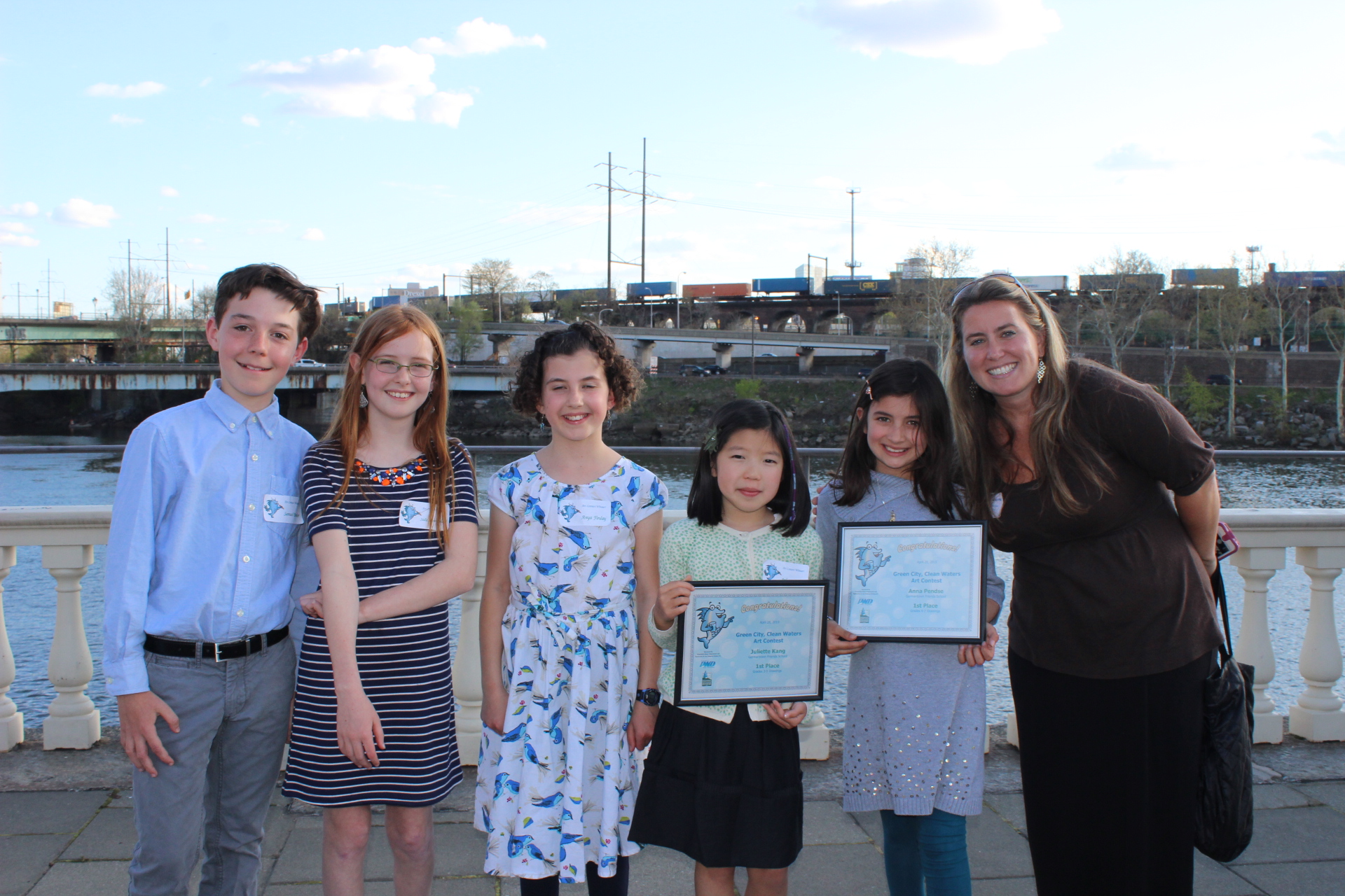 PWD Public Engagement Team Manager Tiffany Ledesma poses with the young winners of a Green City, Clean Waters art contest, with the Schulkill River in the background.
