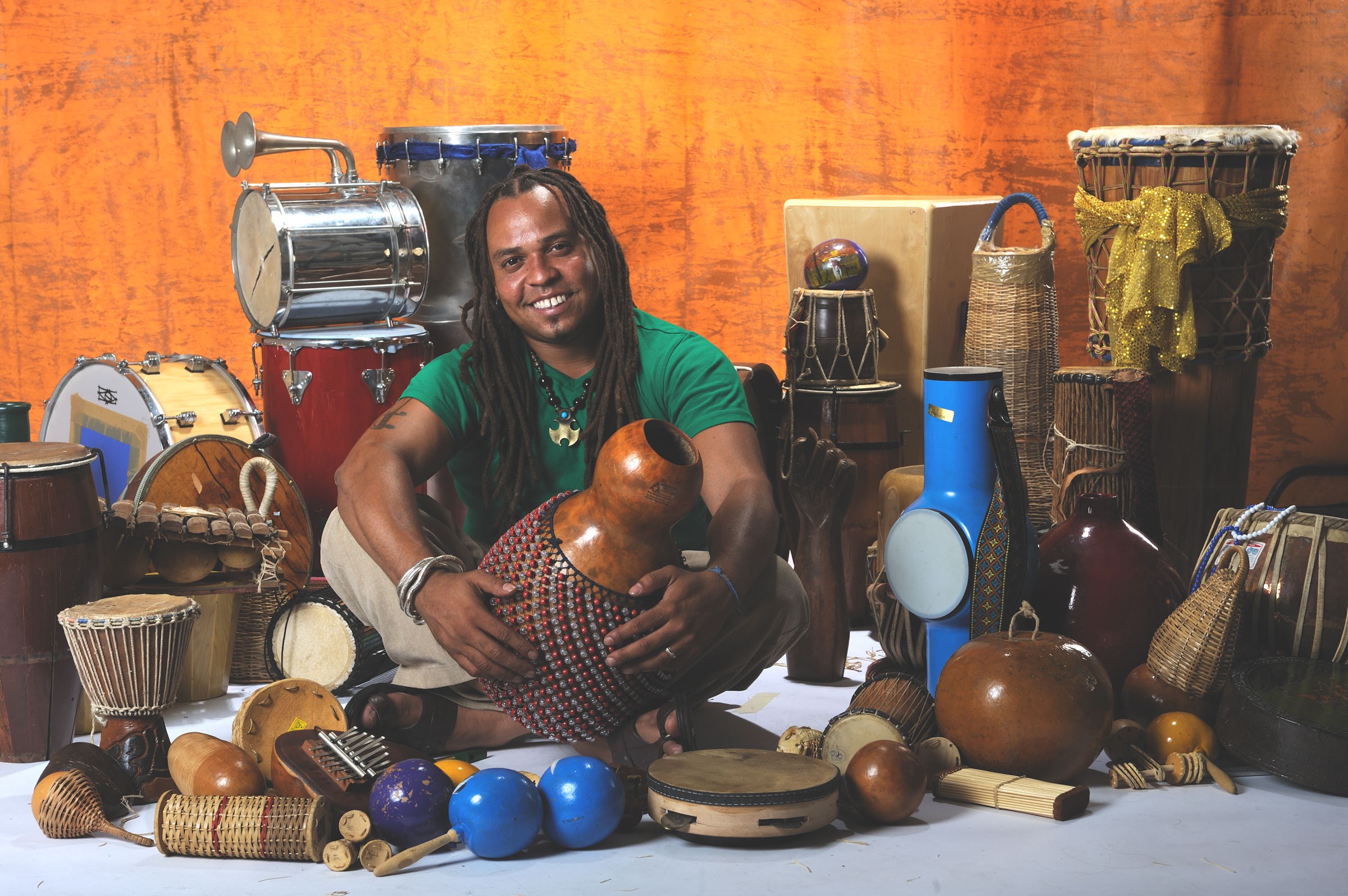 Dendê sits cross-legged, surrounded by various types of hand drums and other small percussion instruments