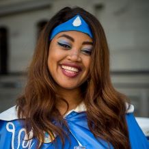 Maura is shown wearing her Water Woman costume with a blue headband and cape, and fabulous eyeshadow to match.