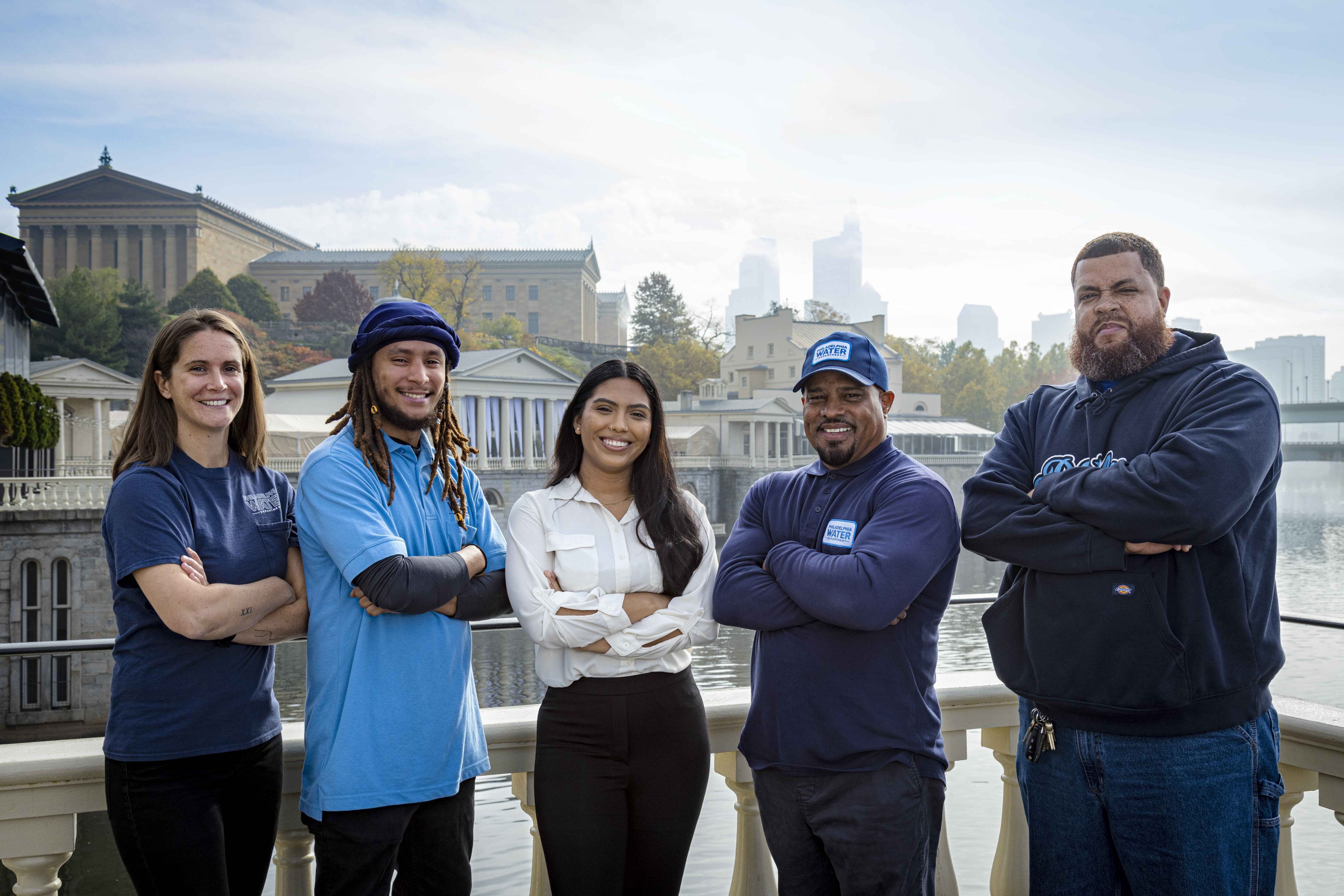 a group of employees from different divisions pose for a photo with the Schuylkill River, Fairmount Water Works, Art Museum, and Philadelphia skyline in the background