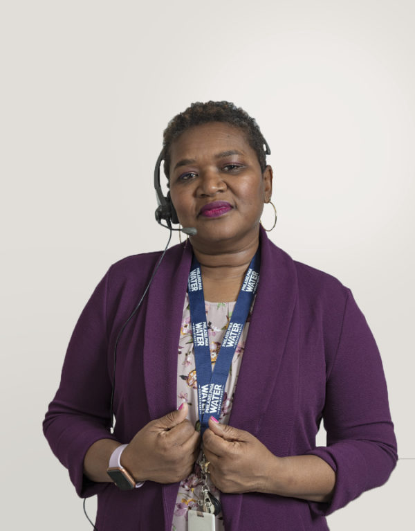A PWD Customer Service Representative is shown from the waist up, wearing a plum-colored cardigan over a light floral blouse, with a headset PWD lanyard, and calm, understanding facial expression.