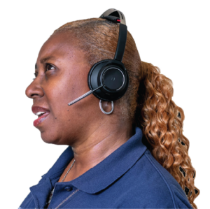 A contact center representative with long curly golden brown hair pulled back into a pony tail, wearing a dark blue polo, silver necklace and hoop earrings, and a phone headset is shown in profile, looking upward with her mouth partially open as if mid-sentence.