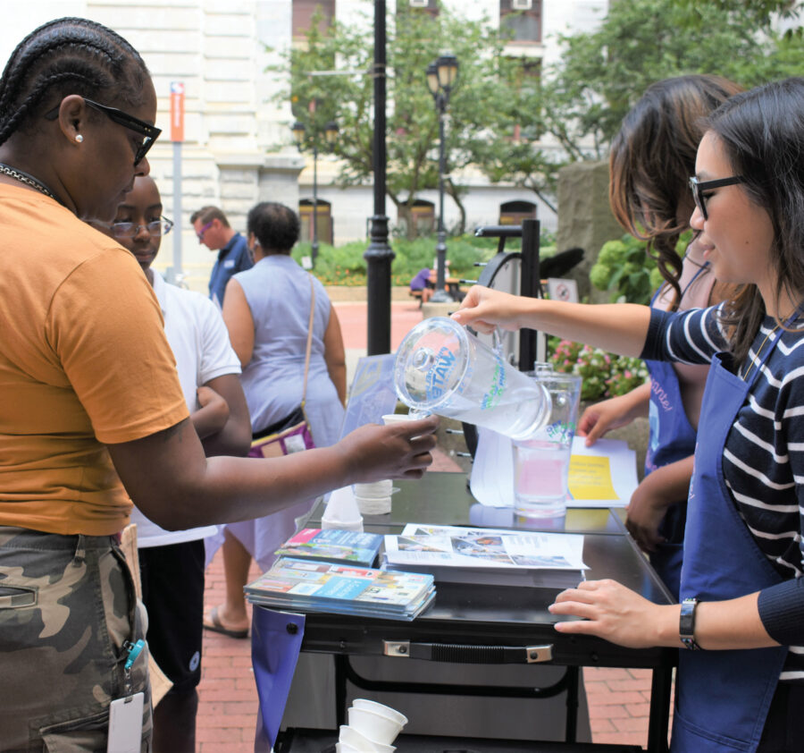 A "bartender" at a Philly Water Bar pop-up event pours a cup of frosty-cold fresh Philly tap water for a passer-by.