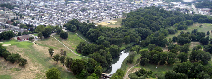 Color aerial image of a small river or creek surrounded by trees with rolling hills and houses in the distance