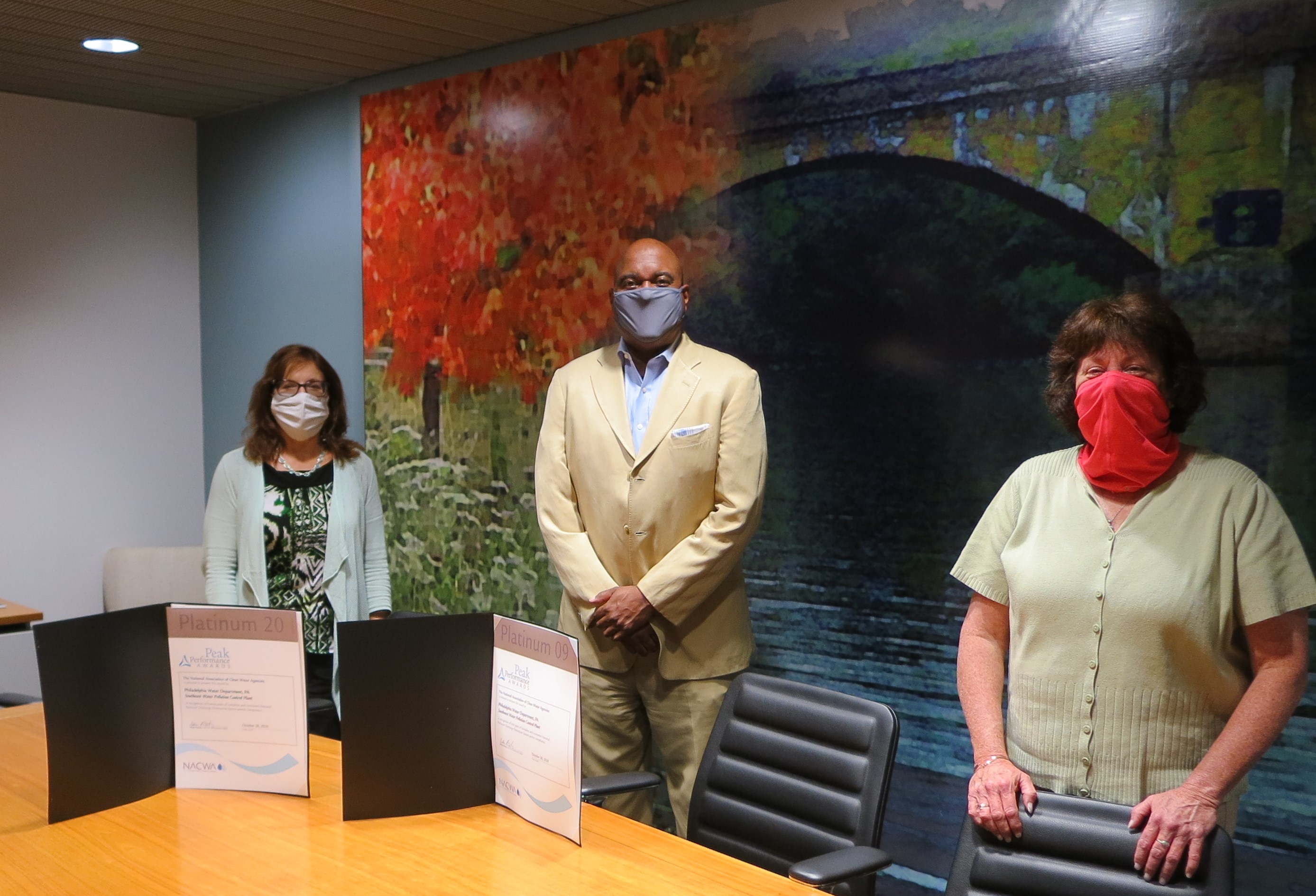 Mary Ellen Senss, Commissioner Hayman, and Donna Schwartz stand spaced out behind a conference table, wearing masks. The award certificates are propped up on the table in front of them.