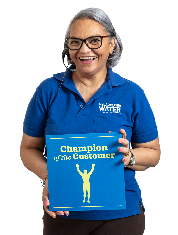 A smiling PWD Contact Center representative with chin-length straight silver hair, wearing a headset, black glasses, a blue PWD polo shirt, and black slacks holds up a card that reads, "Champion of the Customer", with a silhouette of a person standing with arms raised.