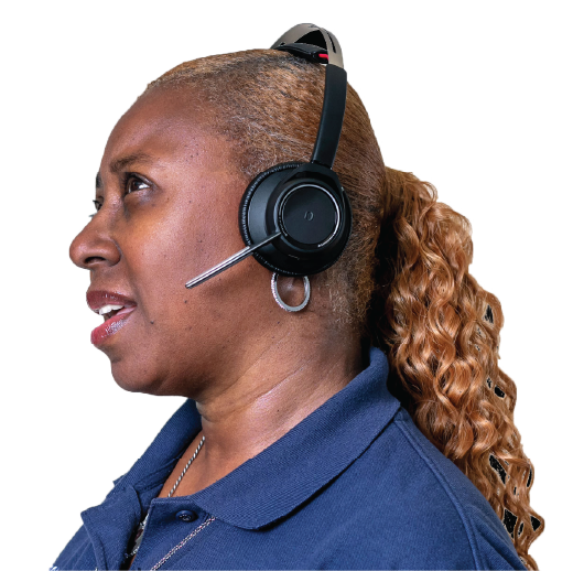 A contact center representative with long curly golden brown hair pulled back into a pony tail, wearing a dark blue polo, silver necklace and hoop earrings, and a phone headset is shown in profile, looking upward with her mouth partially open as if mid-sentence.