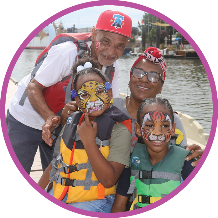 A family wearing lifejackets pose at Delaware RiverFest showing off the kids' facepaint. The river and edge of a boat are visible behind them.