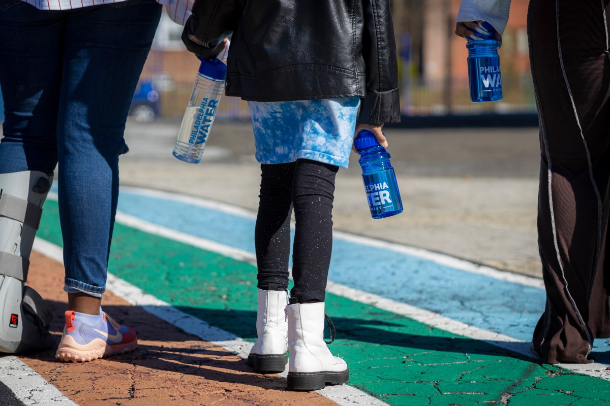 Three kids walking away from the camera on colorfully painted concrete, each holding a reusable water bottle with the PWD logo on it.