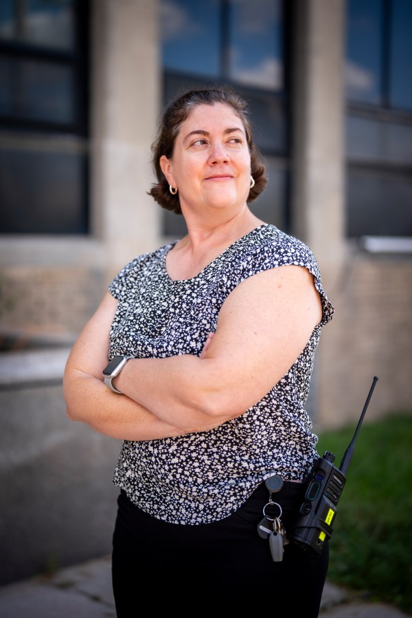 The manager of one of our Water Treatment Plants stands outside the building wearing a black and white floral blouse, keys and radio clipped to her hip pocket, with her arms crossed as she looks off into the distance.