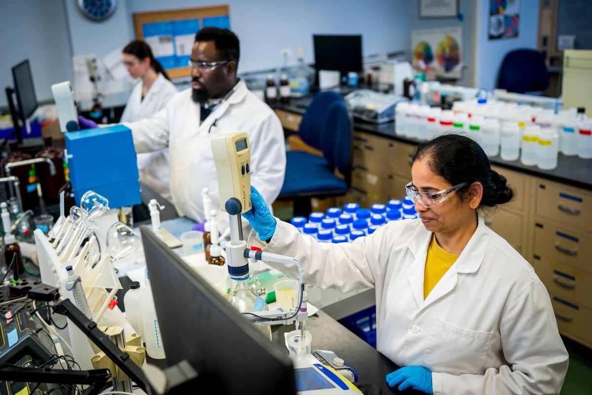 Three PWD scientists in our lab, all wearing white lab coats, safety glasses, and disposable gloves, analyze water samples.