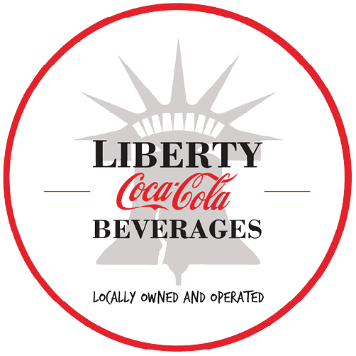 Liberty Coca Cola Beverages logo includes the red script Coca Cola logo, with "LIBERTY" above and "BEVERAGES" below in black serif capitals, overlaid on a light gray silhouette that seems to be a combination of of the Statue of Liberty's crown atop the Liberty Bell. Below, in small casual font reads "Locally owned and operated", and the whole thing is enclosed by a thin red circle.