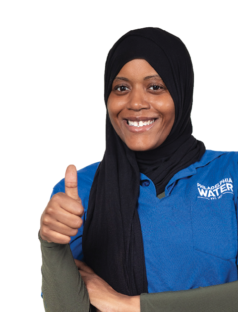 A smiling woman wearing a black head scarf and royal blue PWD polo over an olive green dress gives a thumbs-up.