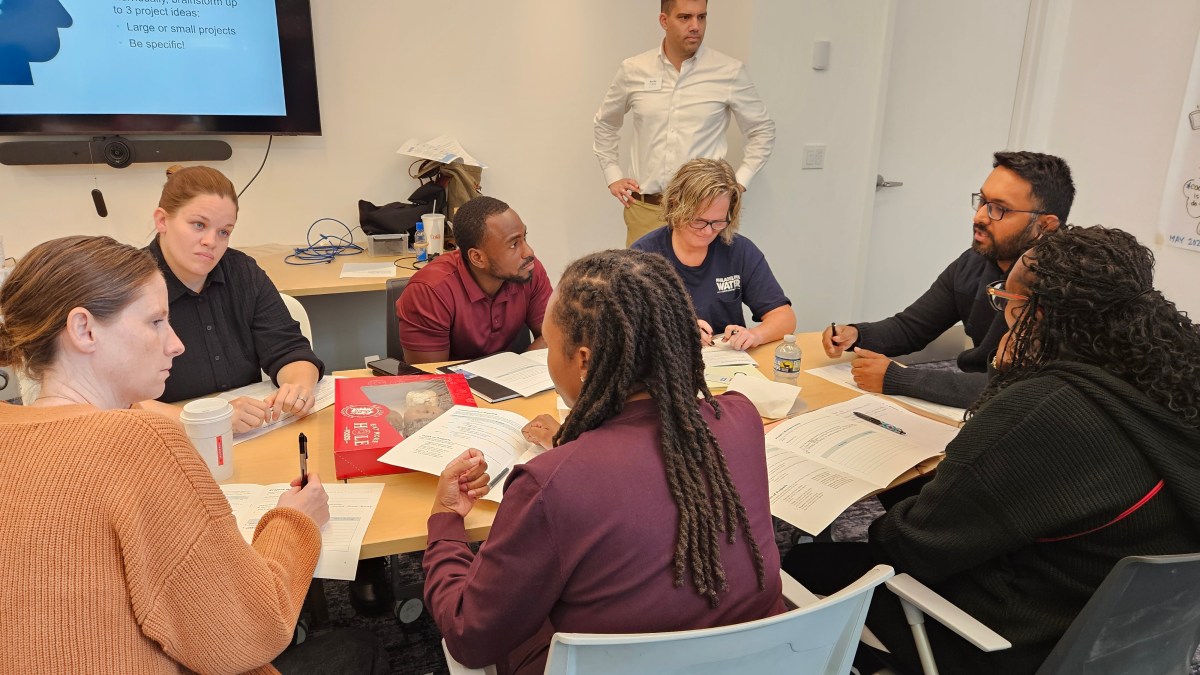 A group of employees in conversation around a conference table, some taking notes.