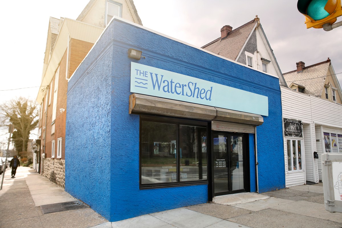 A blocky, 1-story, corner storefront painted a vibrant blue, with a pale blue sign over the door and windows proclaiming it "The Water Shed" in dark blue serif lettering.