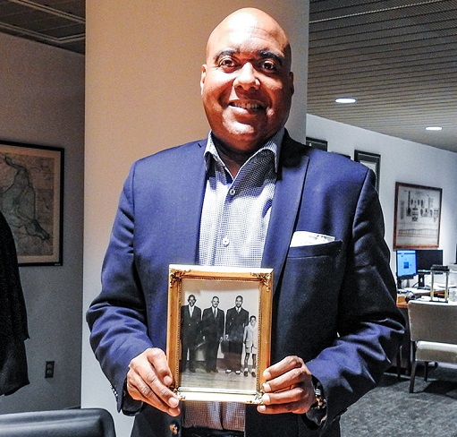 Commissioner Randy E. Hayman holds a photo in his office. It shows four men and a boy, all well dressed in suits except the boy, who has a white shirt with a big collar and shorts. The oldest man is to the left, and it does younger as you go to the right.